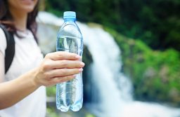 Female tourist holding bottle of clear water on blurred river background